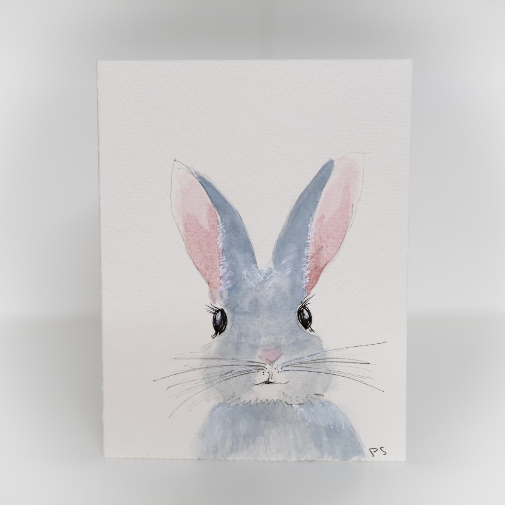 A greeting card featuring a painting of a grey bunny with pink ears.