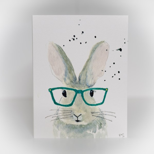 A greeting card featuring a painting of a grey bunny wearing green glasses.