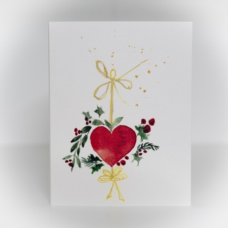 A greeting card featuring a painting of a wreath hanging with a red heart in the middle.