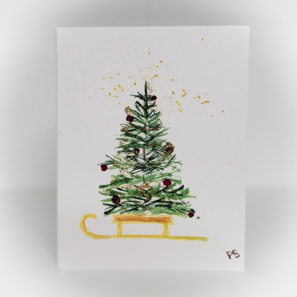 A greeting card featuring a painting of a decorated tree on top of a gold sled.